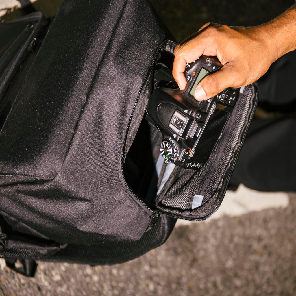 Close up top down view of the Hex Black Cinema Backpack with a person putting a DSLR camera into the camera compartment