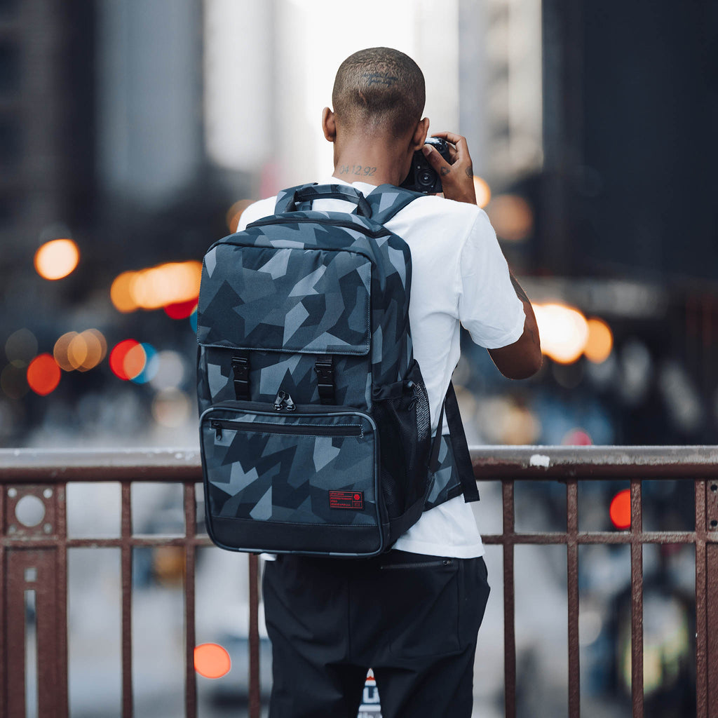 Glacier Cinema Backpack, Grey Camo. Front view. Pack is on a male model in a city setting.